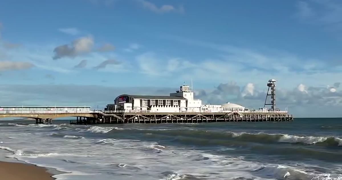 Bournemouth Pier seen from the water&rsquo;s edge on a bright day, with waves breaking in front of it